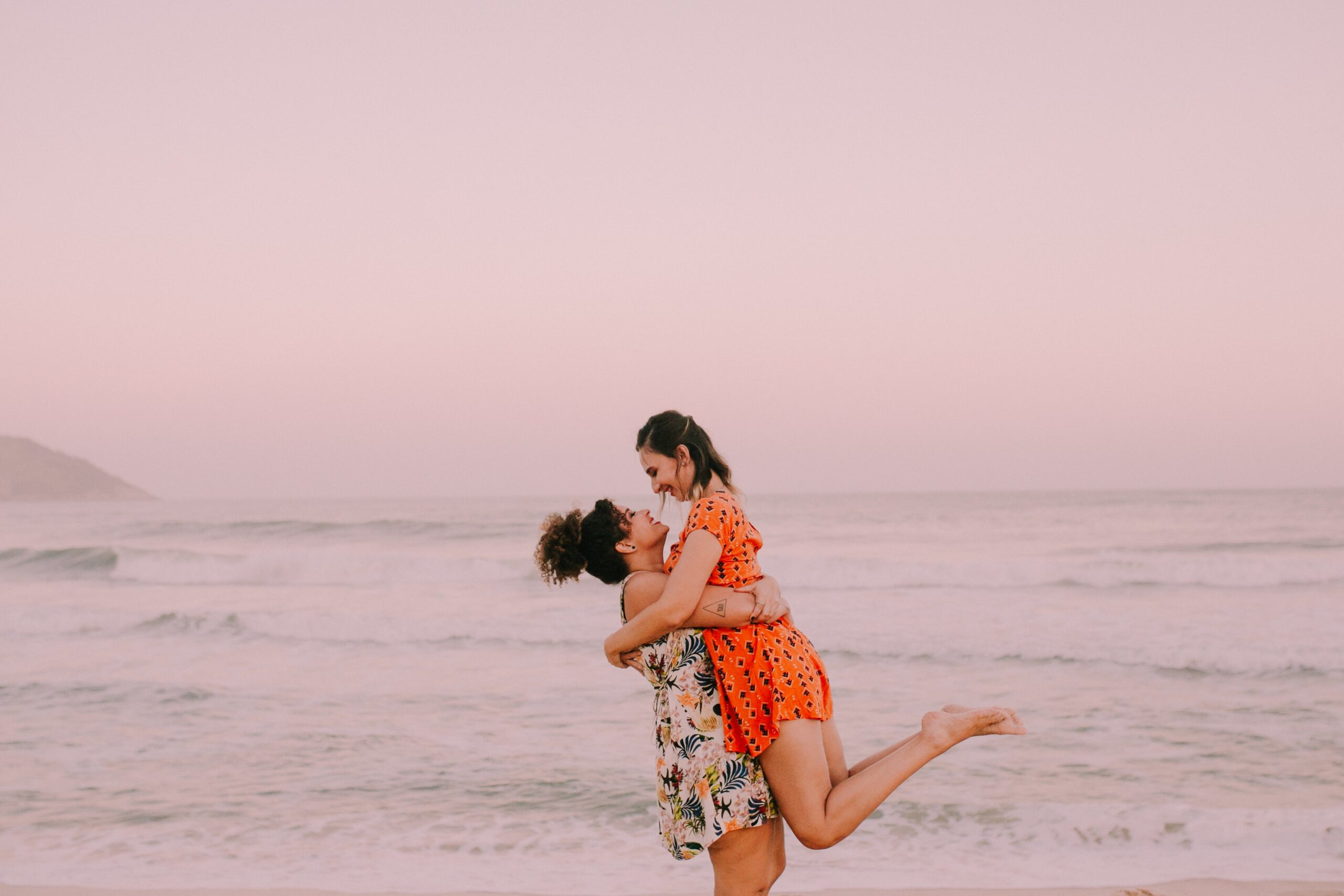 man lifting a woman up in a beach in front of an ocean