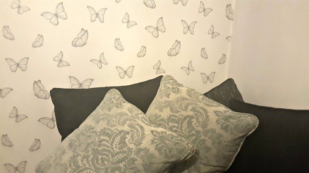 sofa with cushions in front of a white wallpaper with grey sketch butterflies
