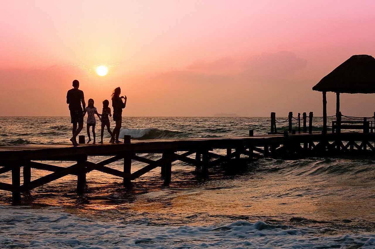holidaying with kids family walking along a pier to a red sunset
