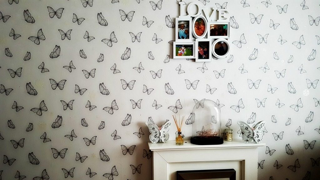 home renovations - white fireplace against white wallpaper with butterflies on and a photo frame hanging above with the word love