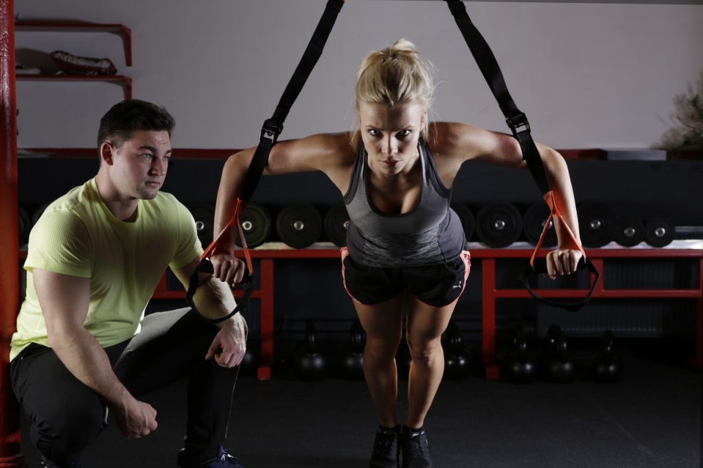 woman using gym equipment with a male personl trainer - getting healthier