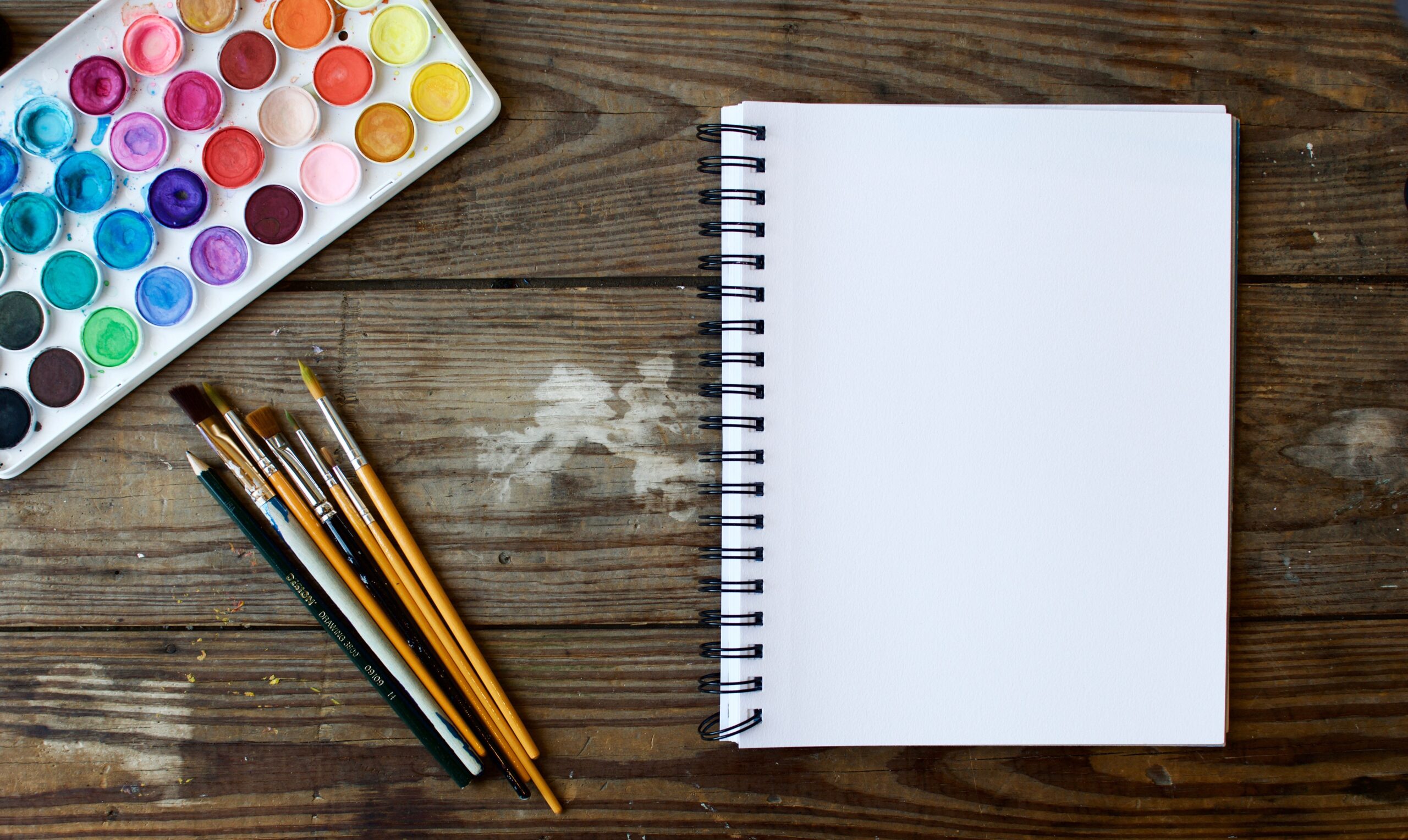 paints paintbrushes and writing pad for post on creative inspiration