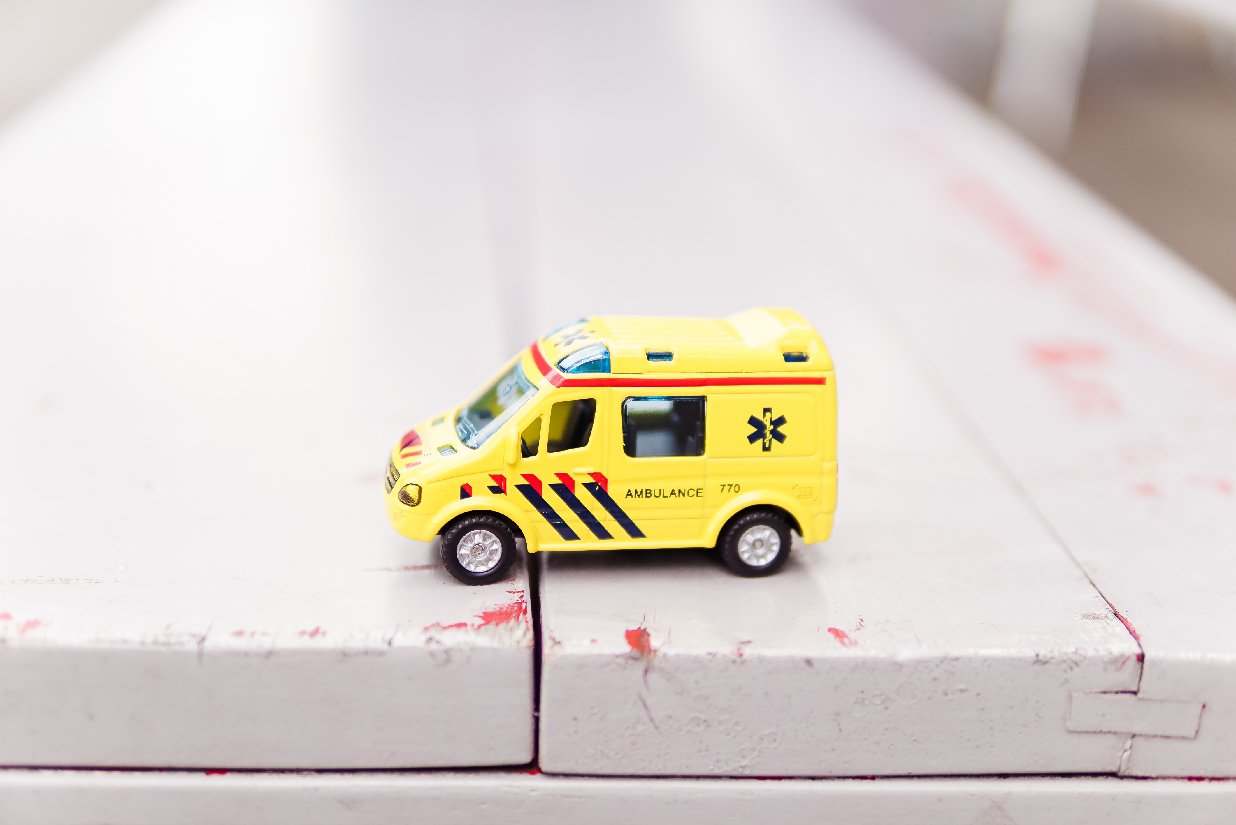 yellow toy ambulance on a white wooden surface