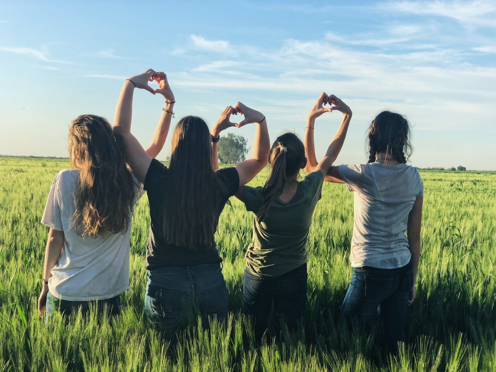 4 women with their backs to the camera linking arms and making heart shapes with their hands