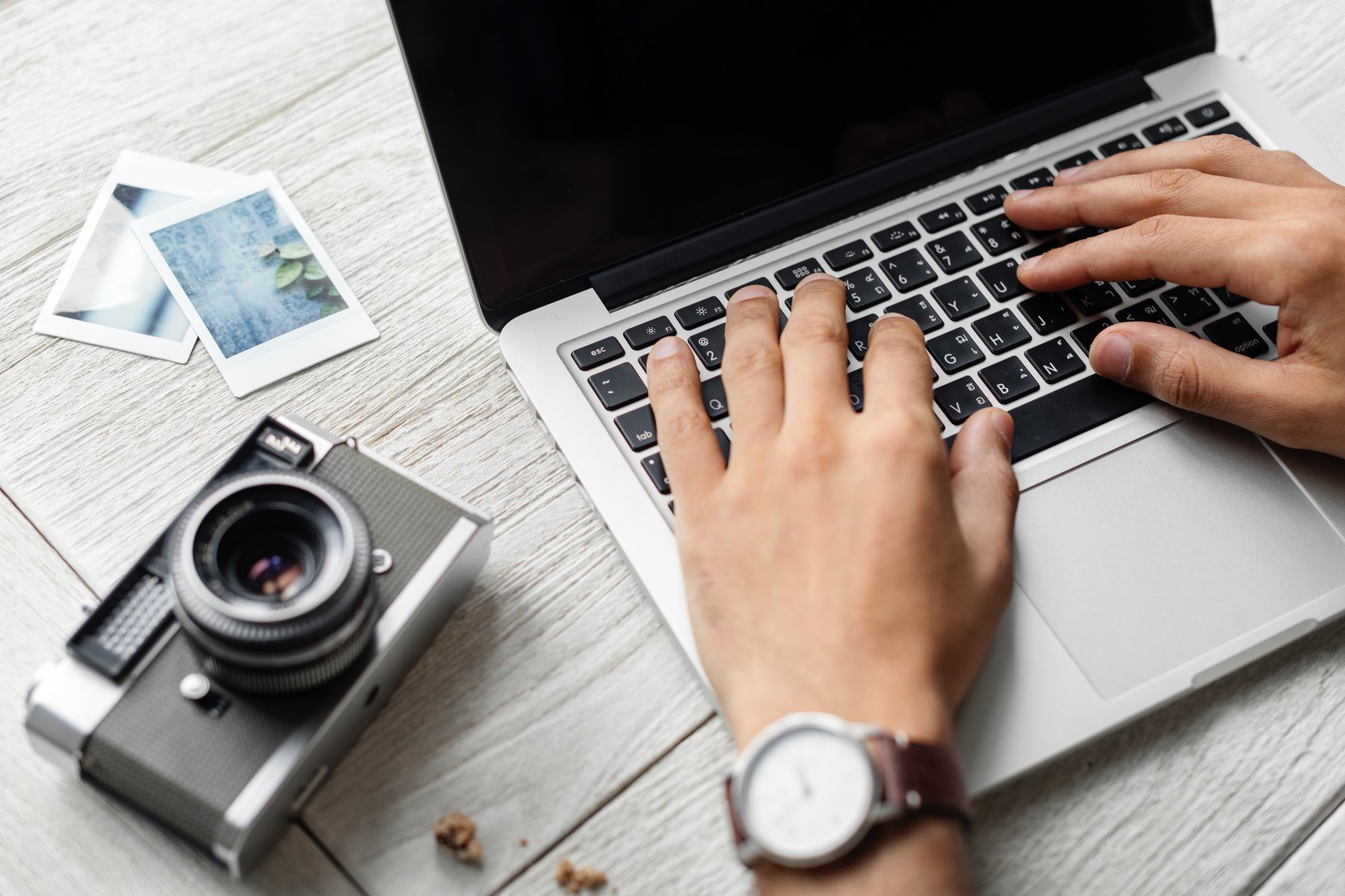 hands on a laptop keyboard with a camera and pictures to one side