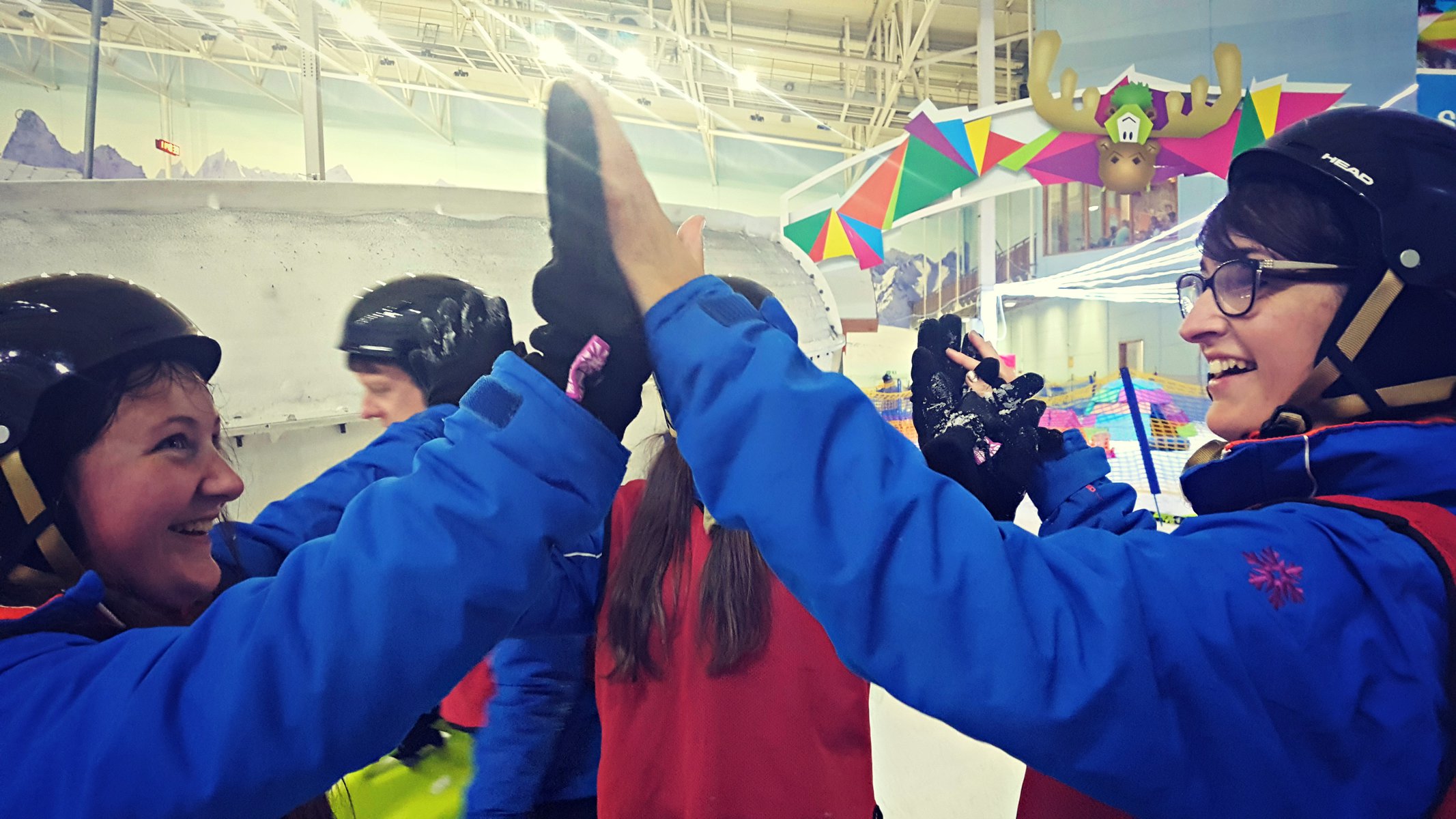 3 girls high fiving wearing snow outfits inside chill factore in manchester