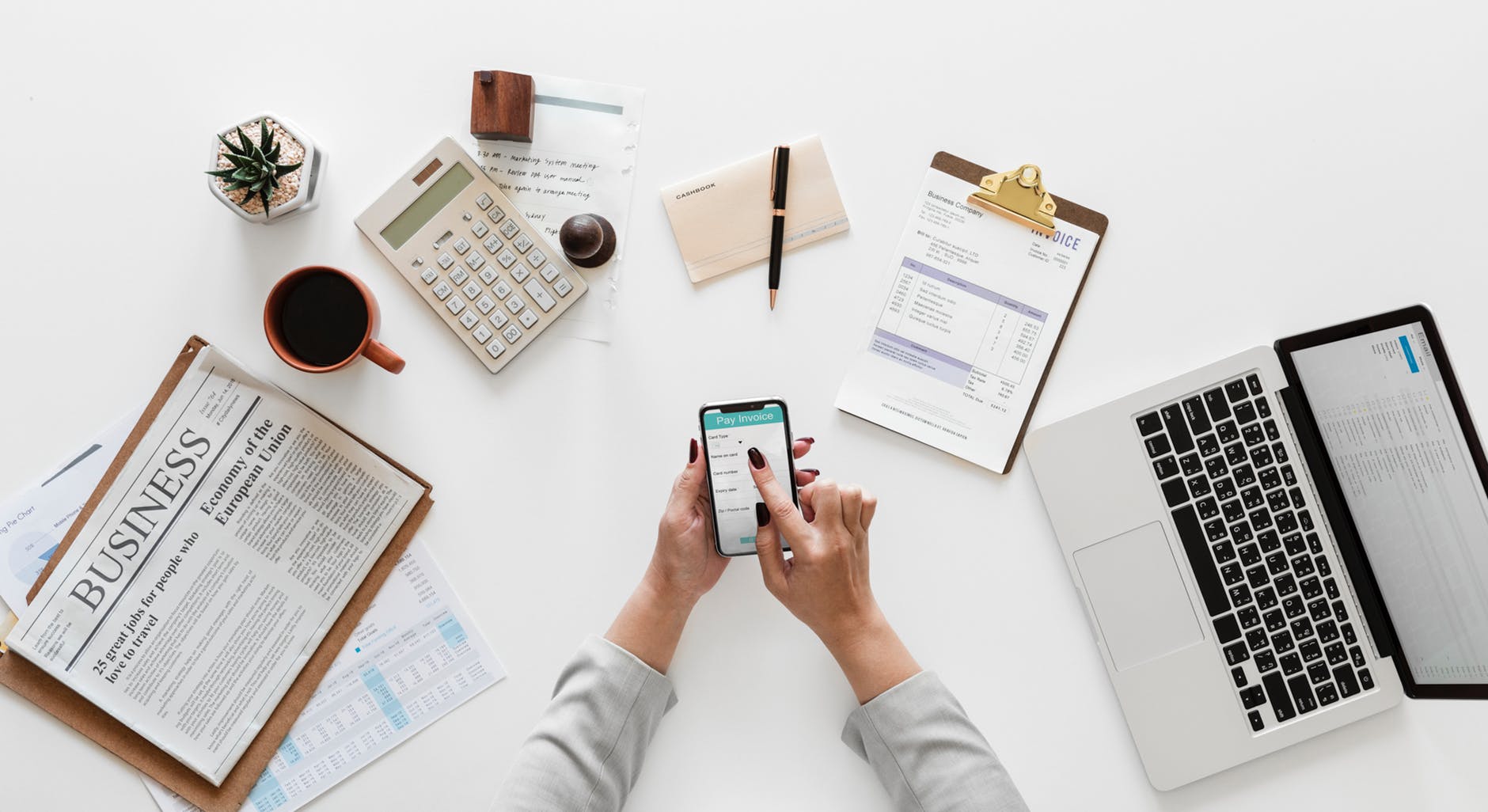 person holding a phone with stationery including calculator, clipboard and pens on a white table