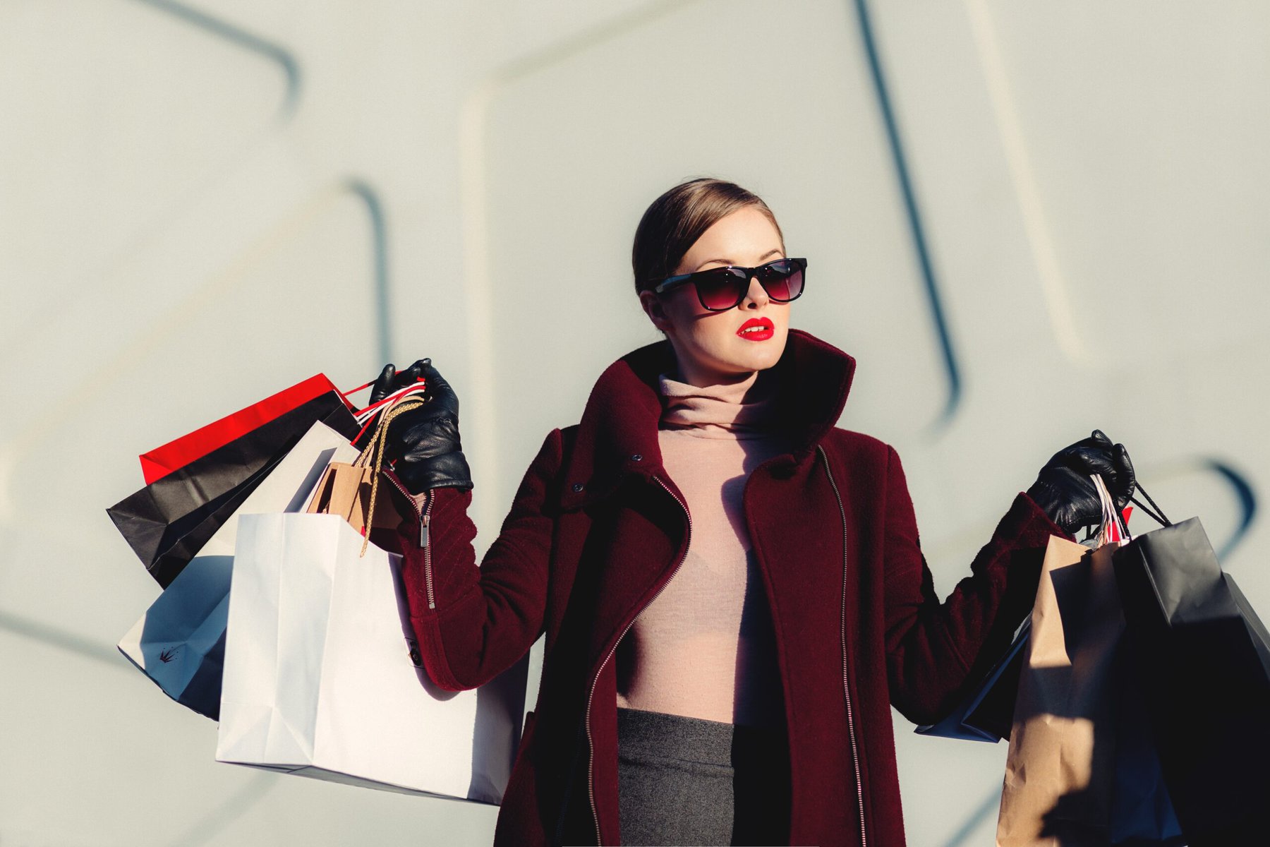 a woman in oversized sunglasses and burgundy coat holding shopping bags