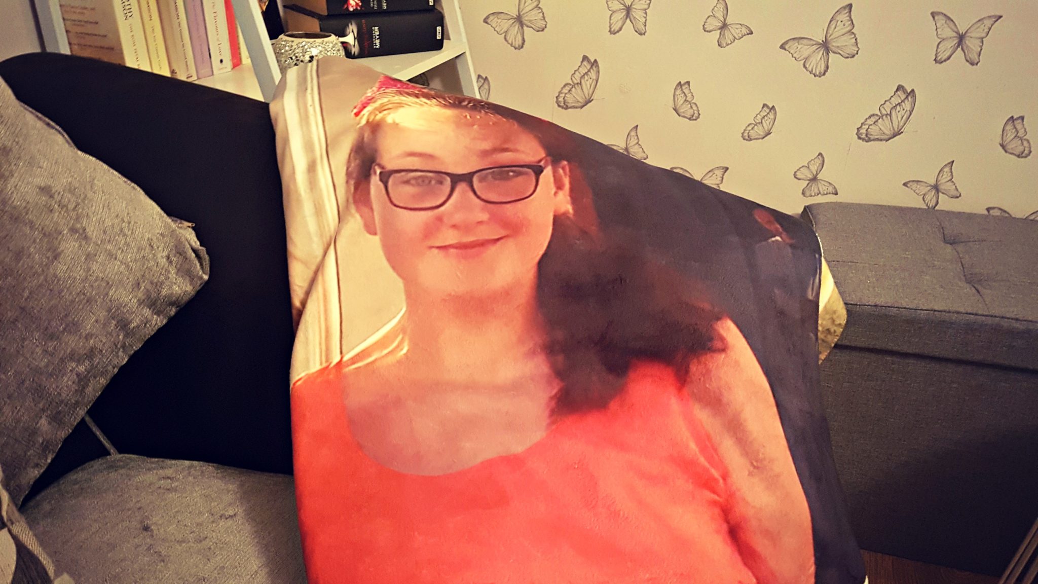 a close of a girl's picture on a photo blanket draped over a grey sofa with butterfly wallpaper in the background