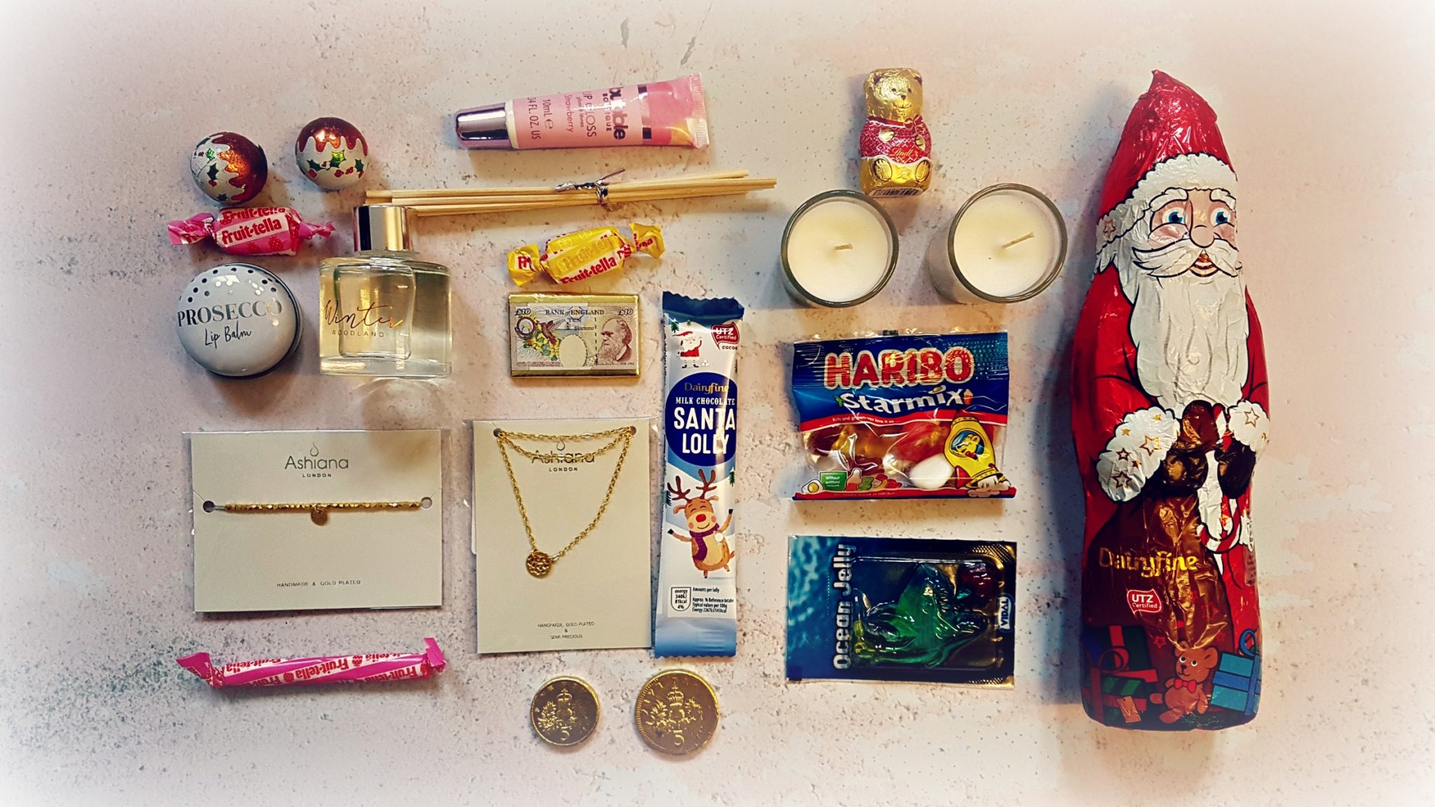 selection of christmas chocolates and sweets with a bracelet, necklace, lip balm and candle related products all arranged in flatlay