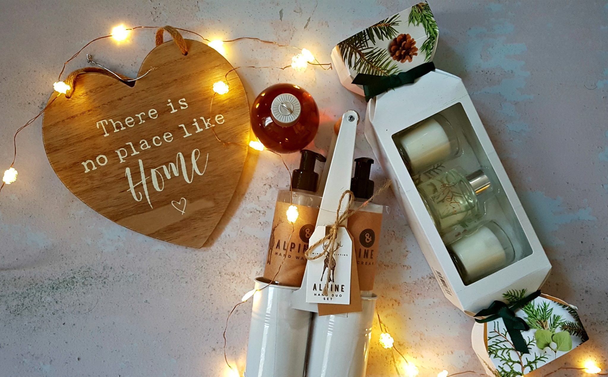 a selection of home bargains christmas gifts including a wooden sign saying there is no place like home, a carry handle tin with hand creams in and a cracker stlye box with candles in and small bottle of bubble bath