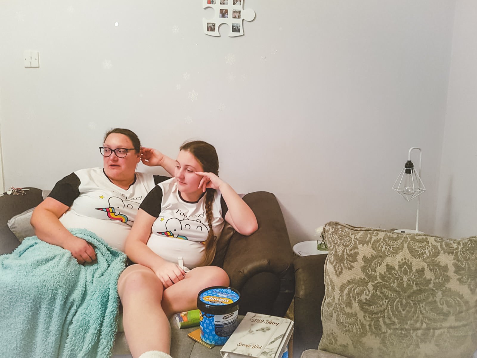 two women sat on a sofa wearing pjs with a duck egg blanket watching tv