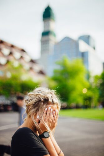 woman with blonde hair in an upstyle with her hands over her face
