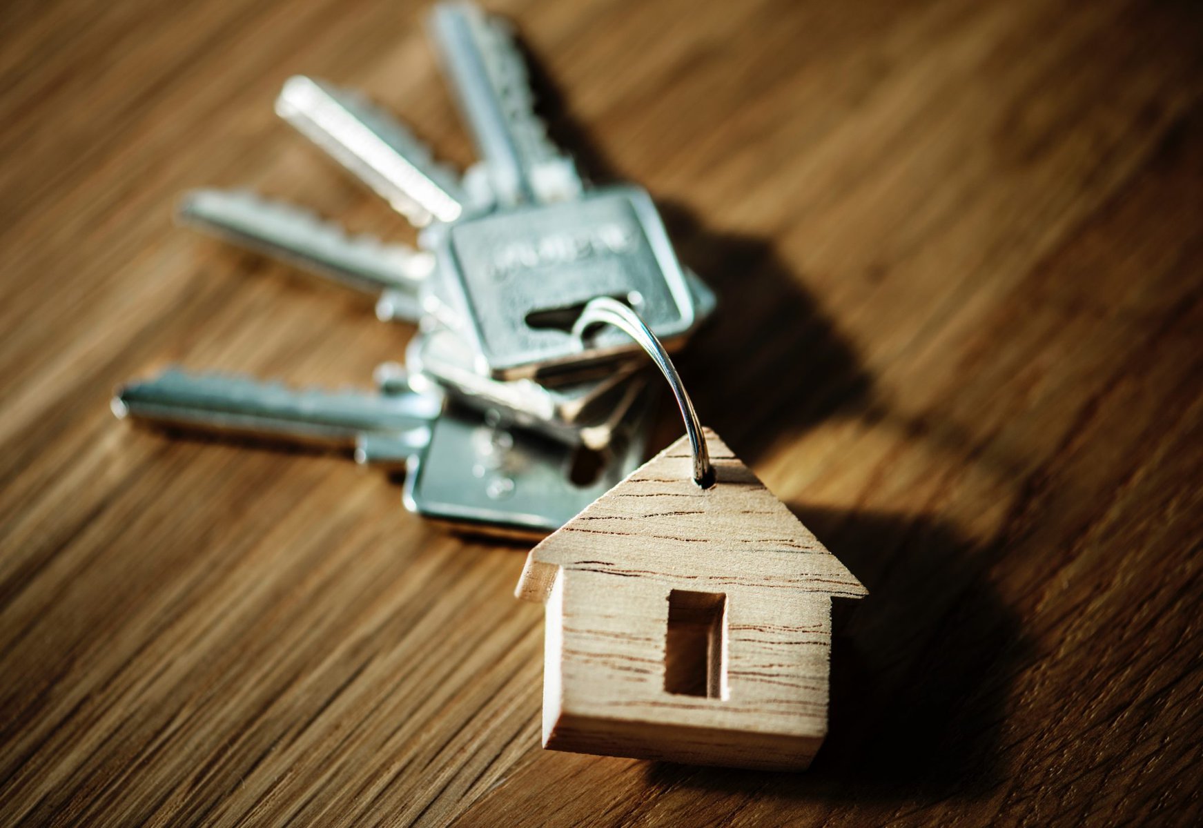 silver keys lying on a wooden background with a wooden house keyring attached