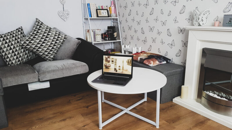 an open laptop on a white table in a living room setting with grey furniture showing the benefits of pilates via your pilates physio online pilates videos
