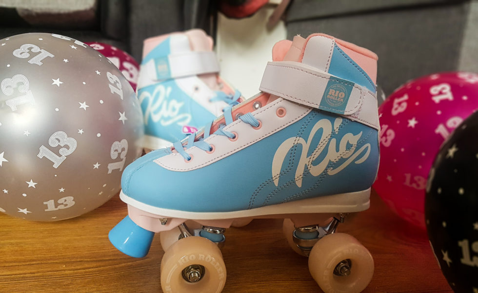 a pir of baby blue and white roller skates on a wooden floor surrounded by pink, grey and black balloons with 13 on them
