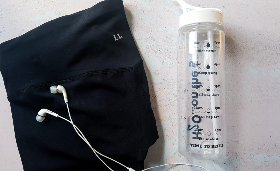 black love leggings sports legging in flatlay with white in ear headphones and a water bottle