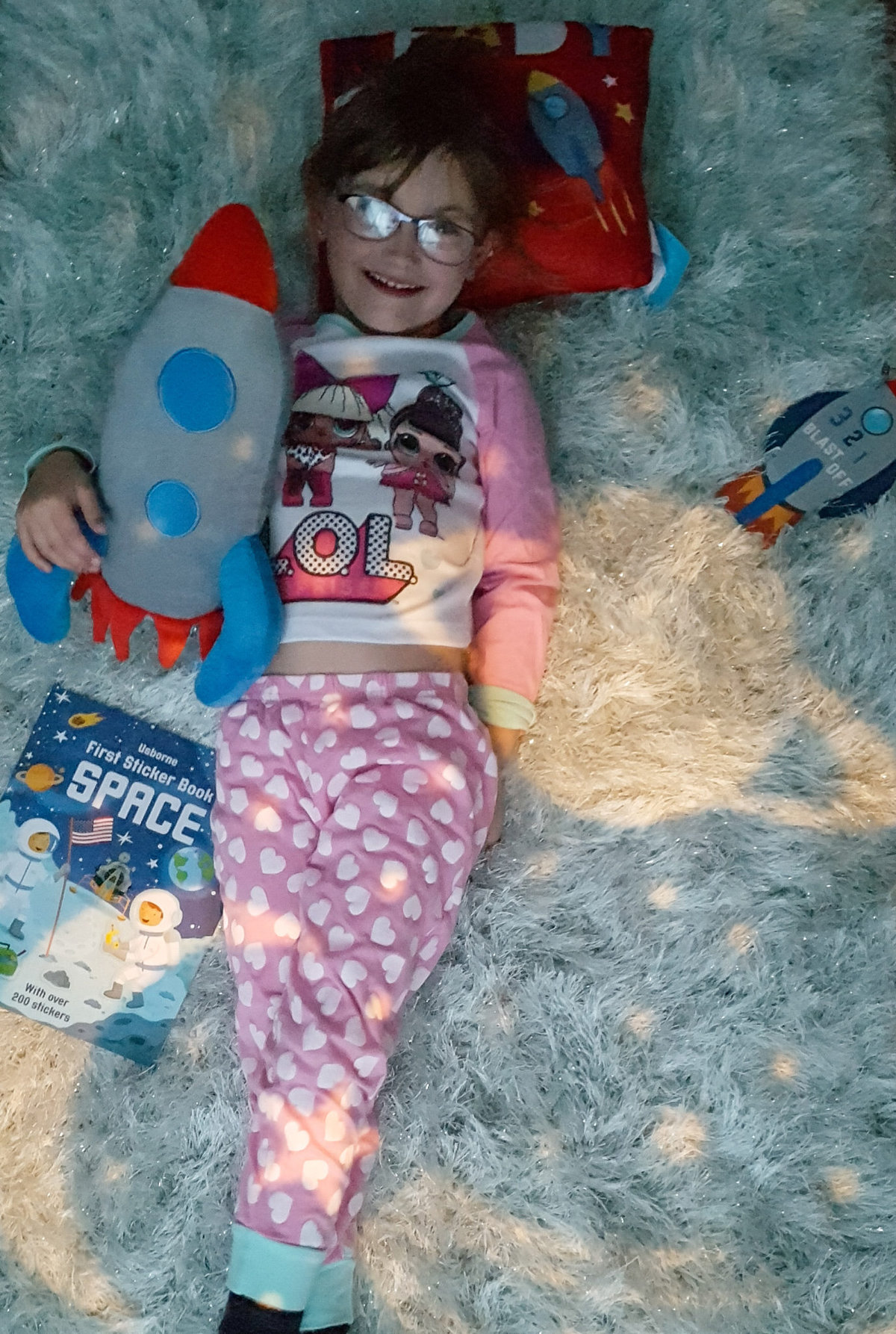 young girl lying on a mint coloured rug with space theme lights and cushions around her