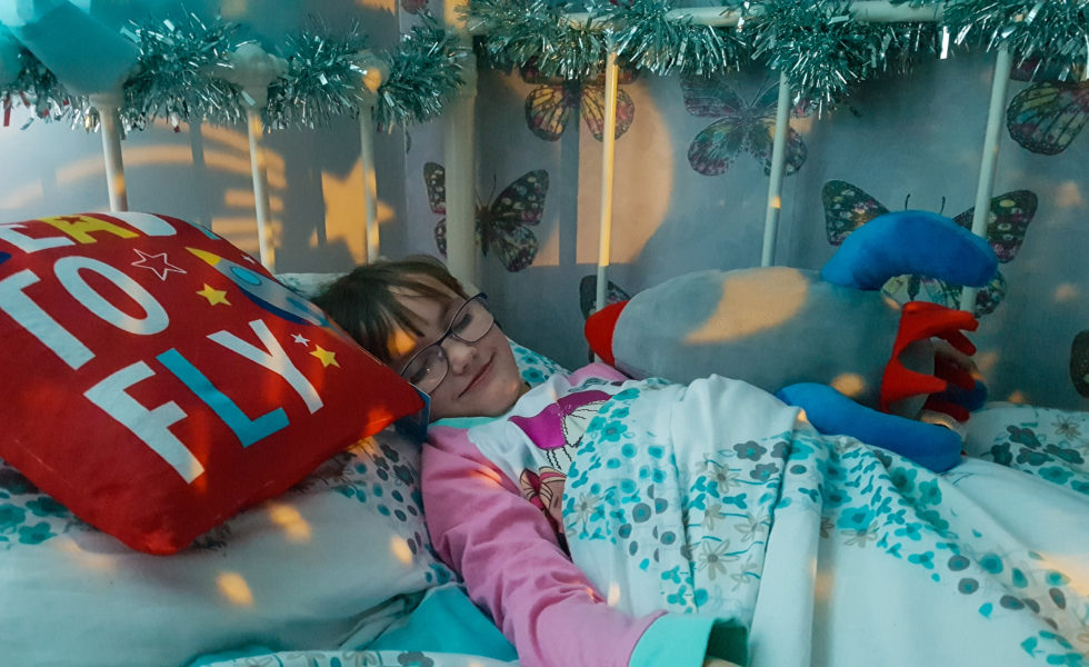 young girl sleeping in bed with light shapes of stars around her and rocket ship cushion