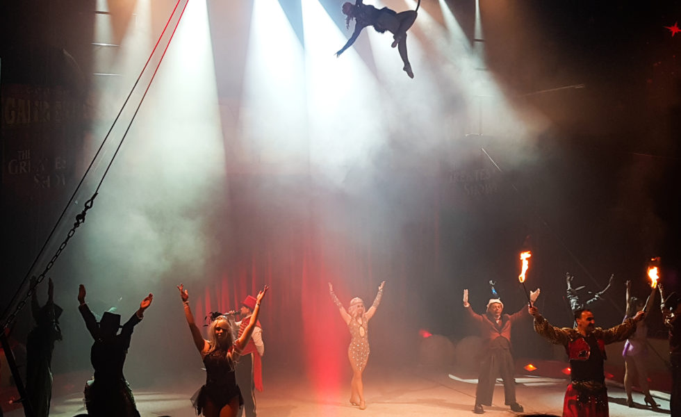 gandeys circus performers stood in a circle with an aerial hoop performer in the air