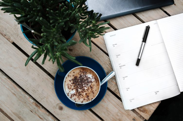 a pen, notebook, coffee cup snd green plant on a wooden desk