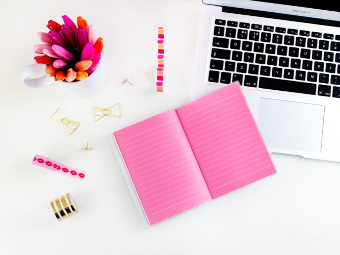 a white desk with white laptop and pink acessories