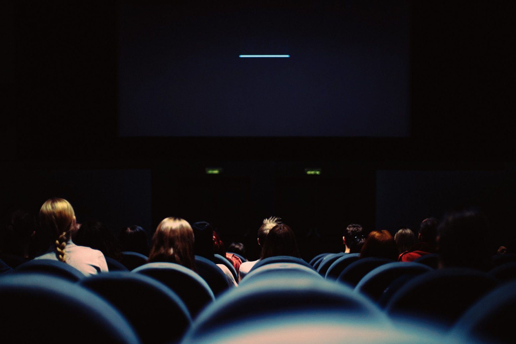 a cinema screening room in the dark showing the backs of chairs