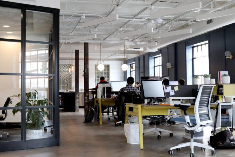 an open plan office with desks and assorted equipment with a person sitting at one of the desks