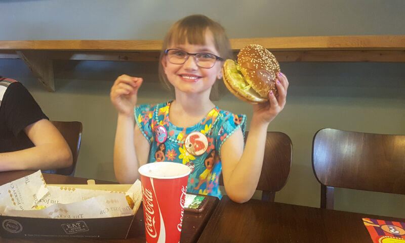 young girl holding a cheeseburger and smiling