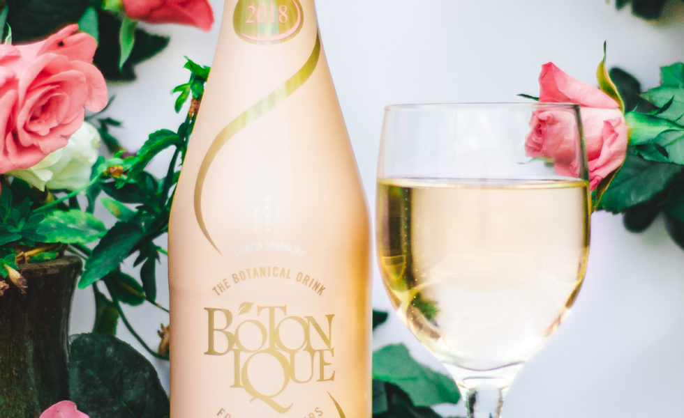 a bottle of blush botonique with a filled glass beside it in a flower arrangement