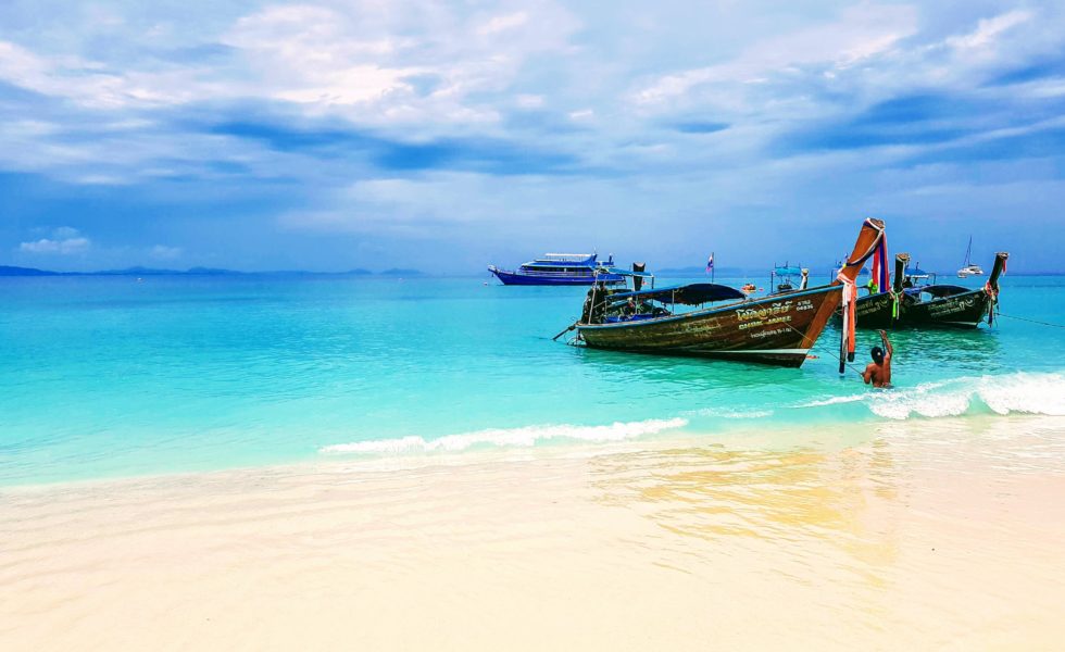 small wooden boats near the shoreline in green seas against a blue sky and yellow sand