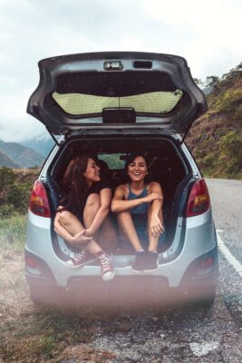 two women sitting in the boot of a car laughing