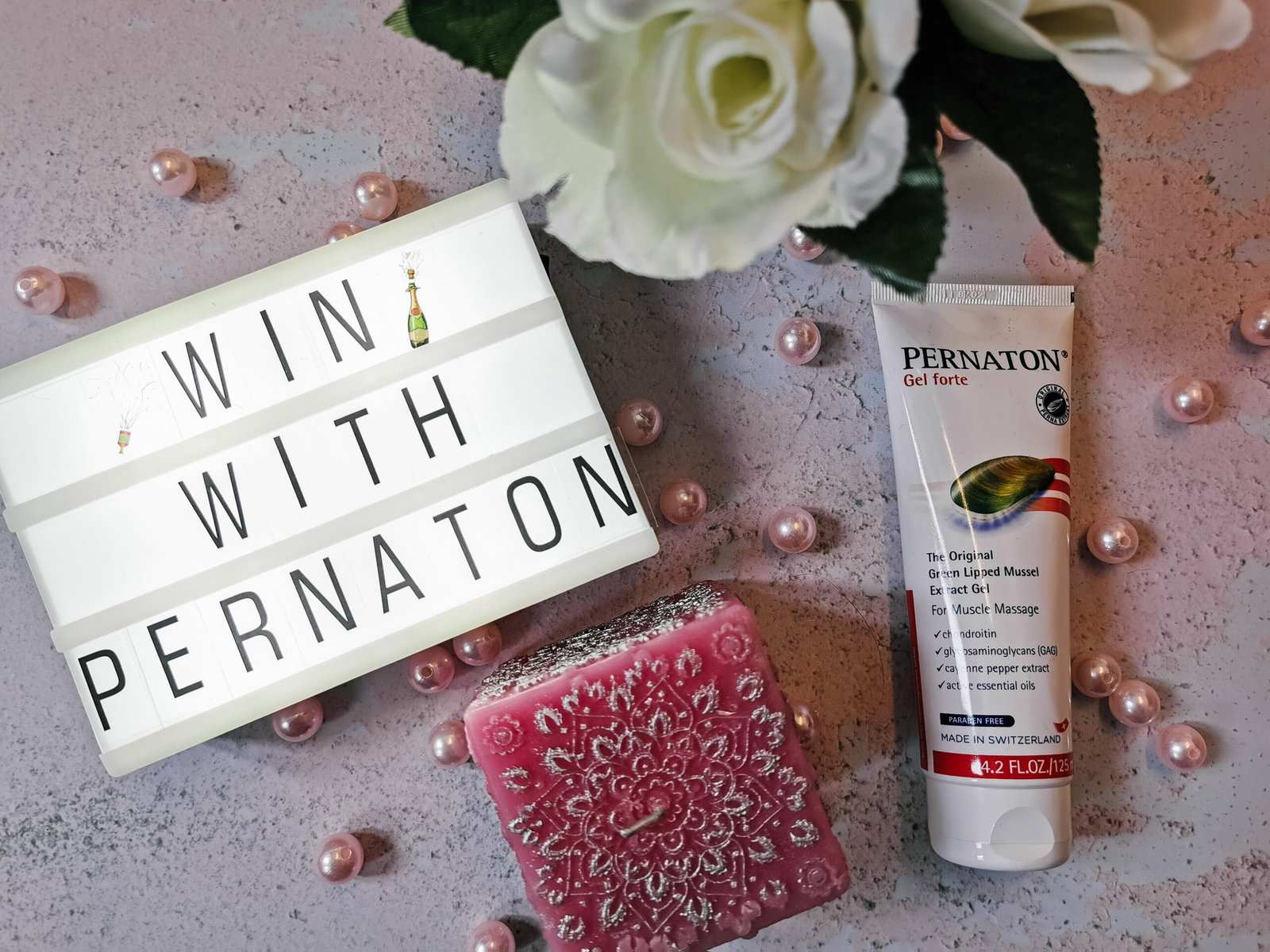 a flatlay image with a lightbox, candle, artifical flowers and a tube of pernanton gel
