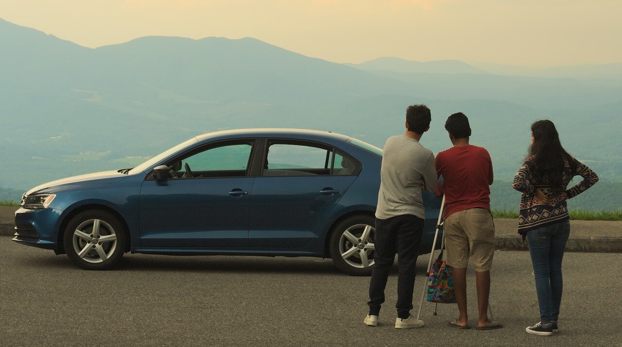 people looking at a blue car with a mountain in the background