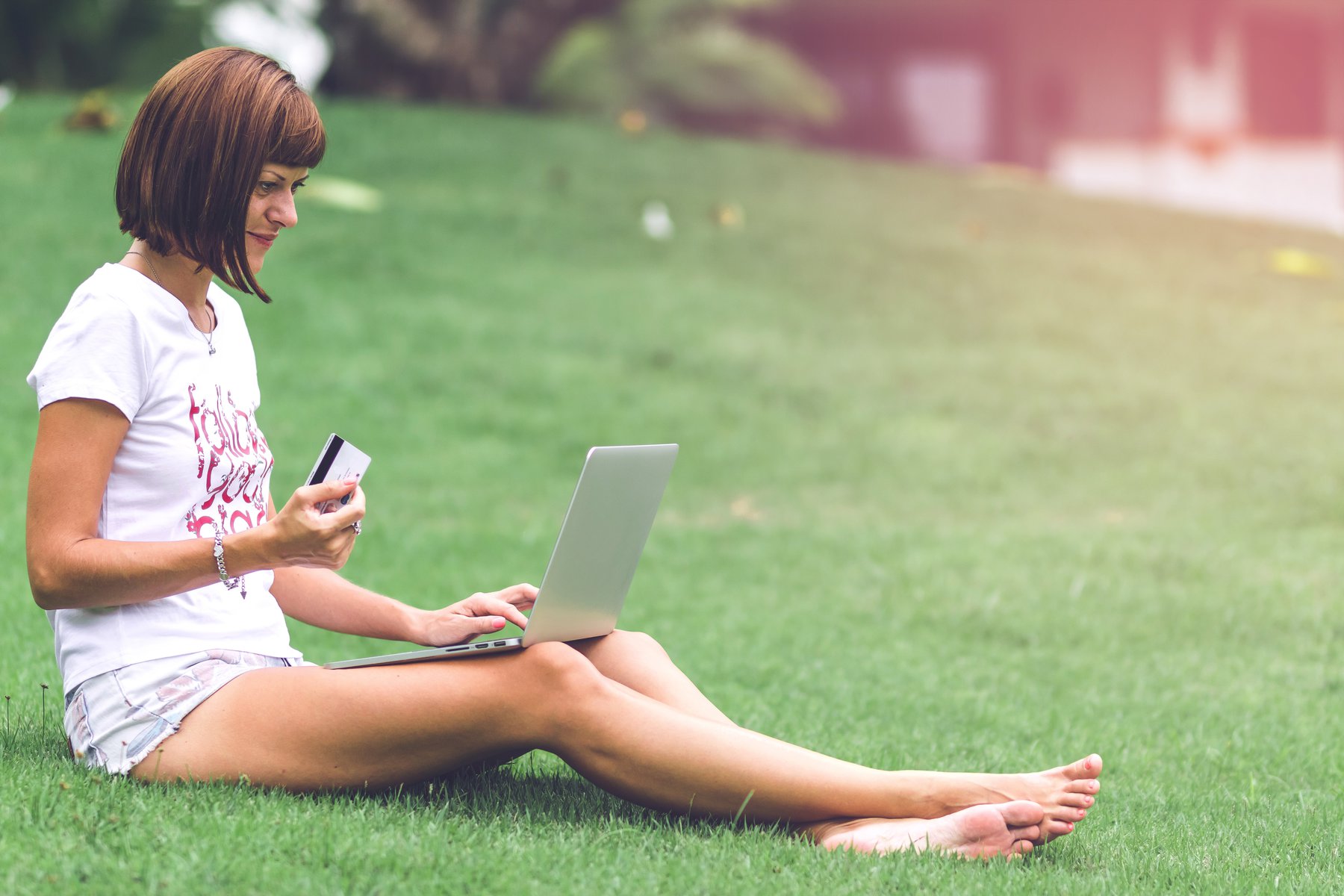 a woman sitting bare foot on grass looking at a laptop