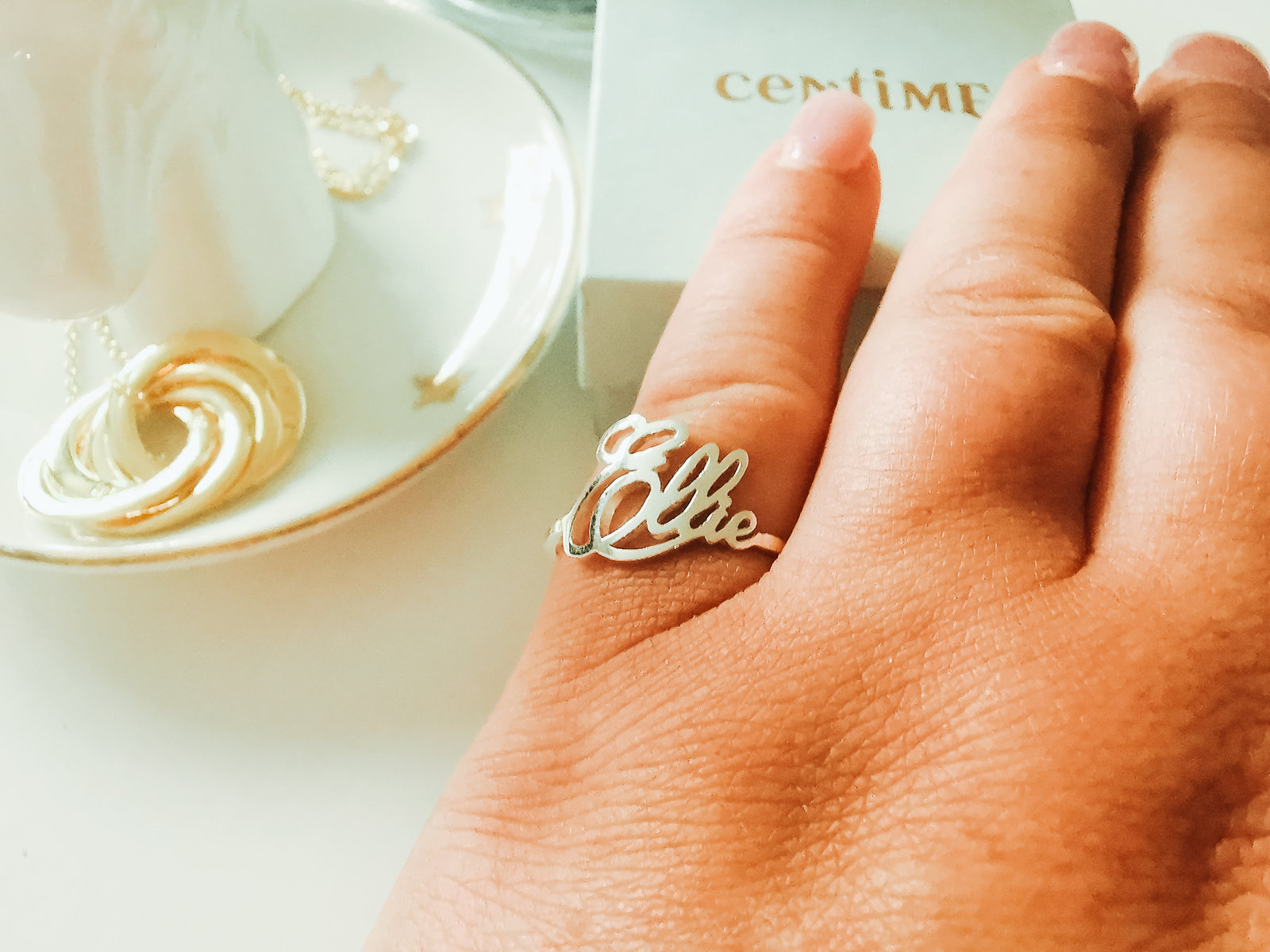 a picture of a womans hand wearing a silver name ring with a gold necklace in the background on a jewellery tray