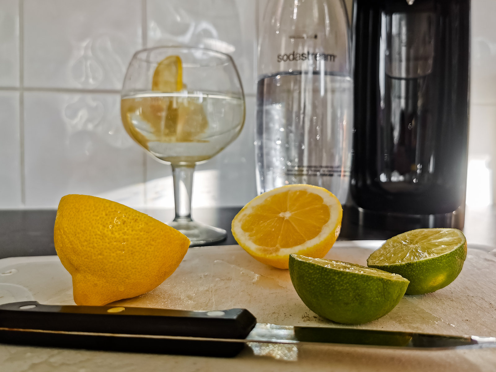 soda stream in background with glass with sparking water in and sliced lemons and limes