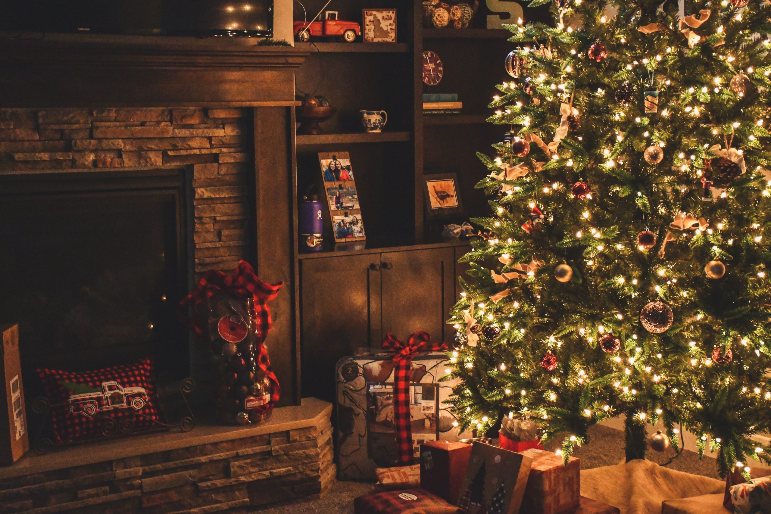 christmas tree with fairy lights on in low light next to a fireplace