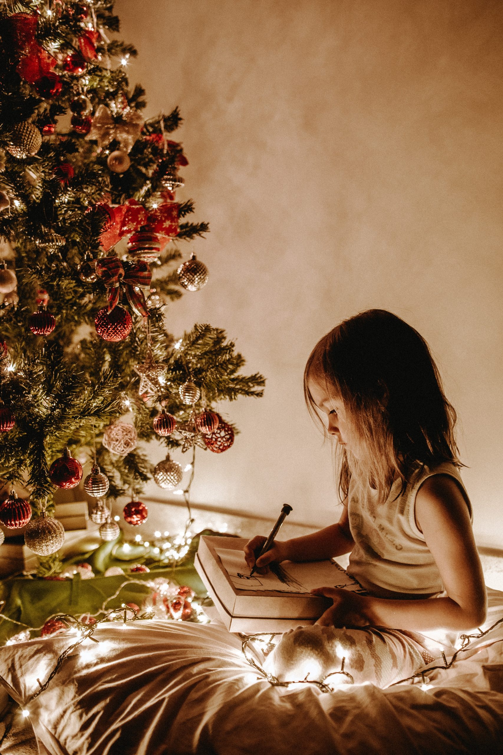 girl sitting near a christmas tree with twinkling lights on