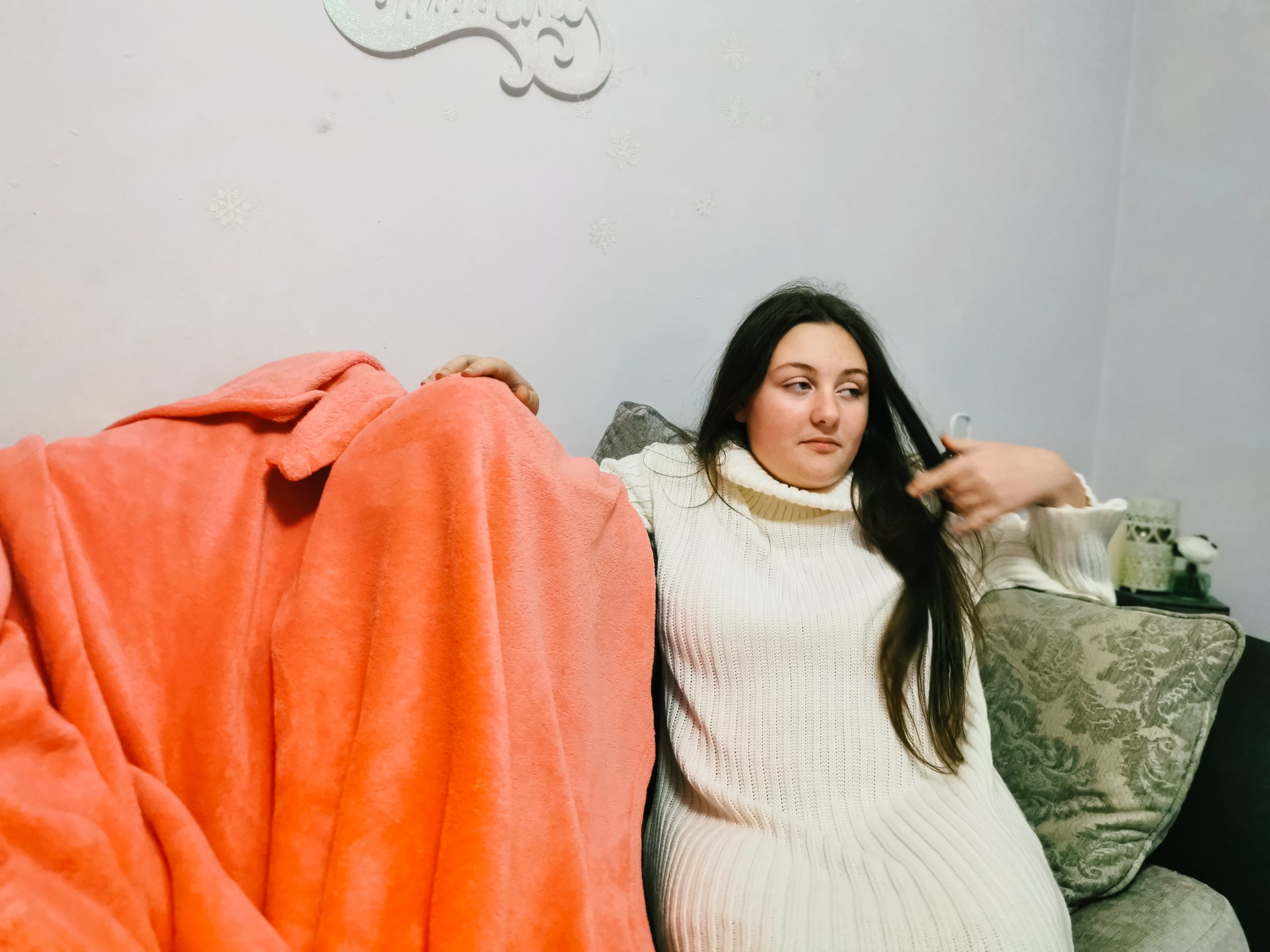 young girl wearing a cream sweater dress sitting on a sofa