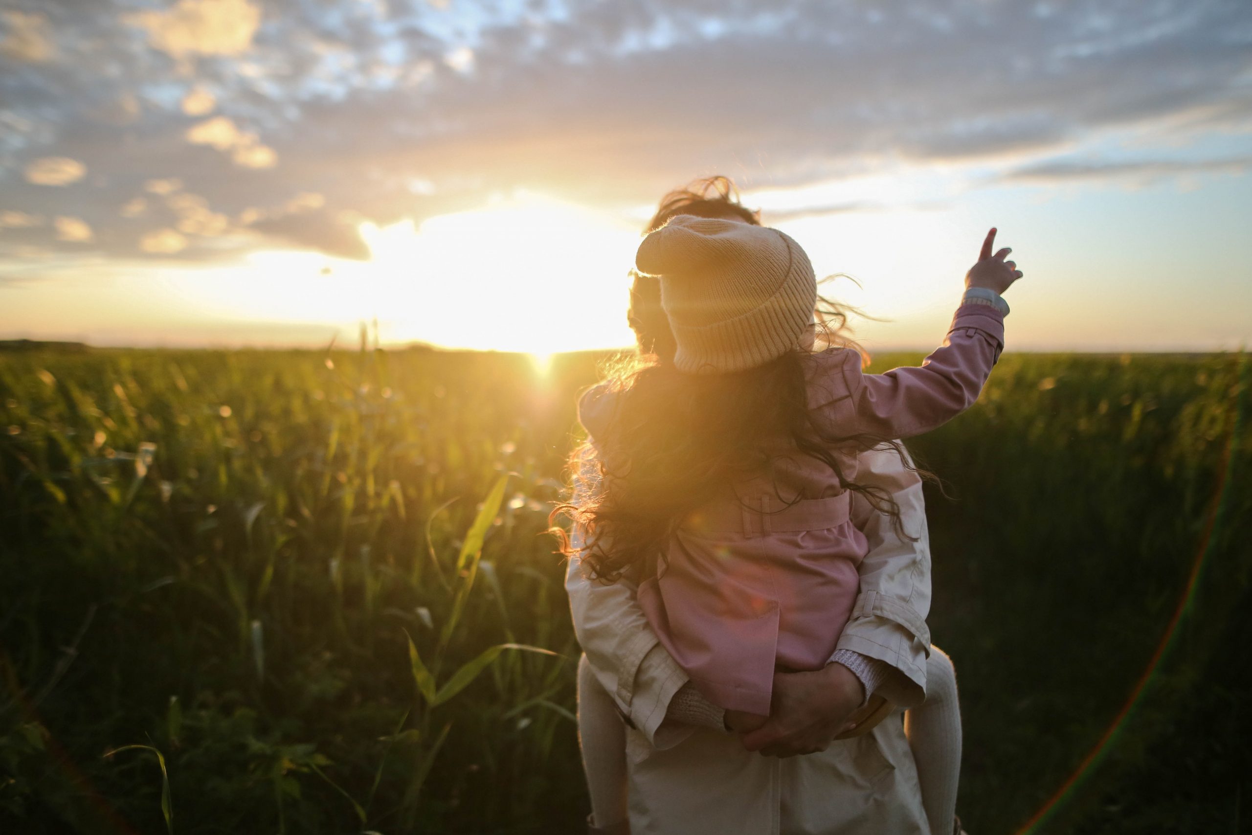 mother and daughter on grass in front of a setting sun