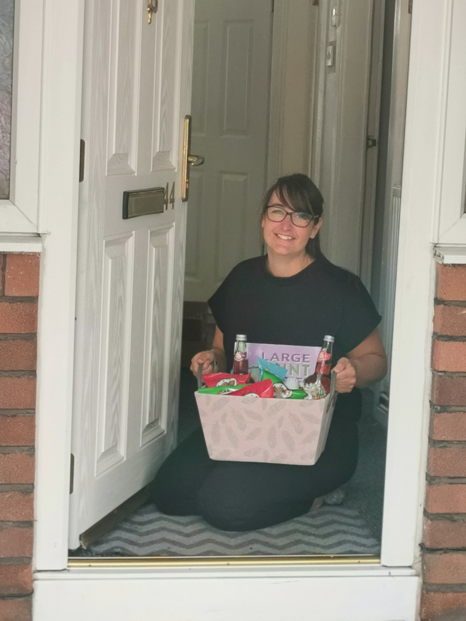 woman kneeling down holding gift basket at a front door