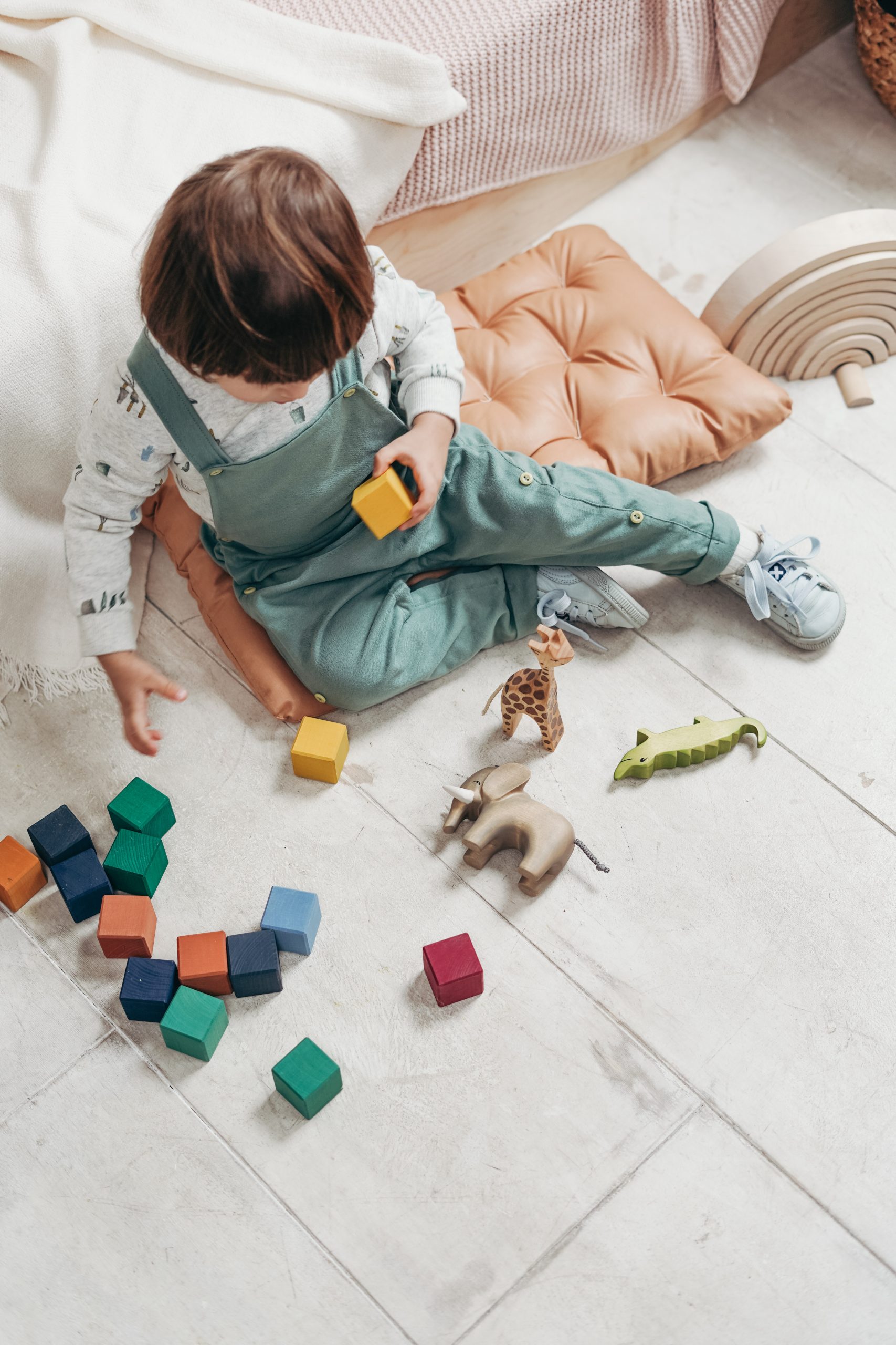 child in dungarees playing on a white floor with wooden toys