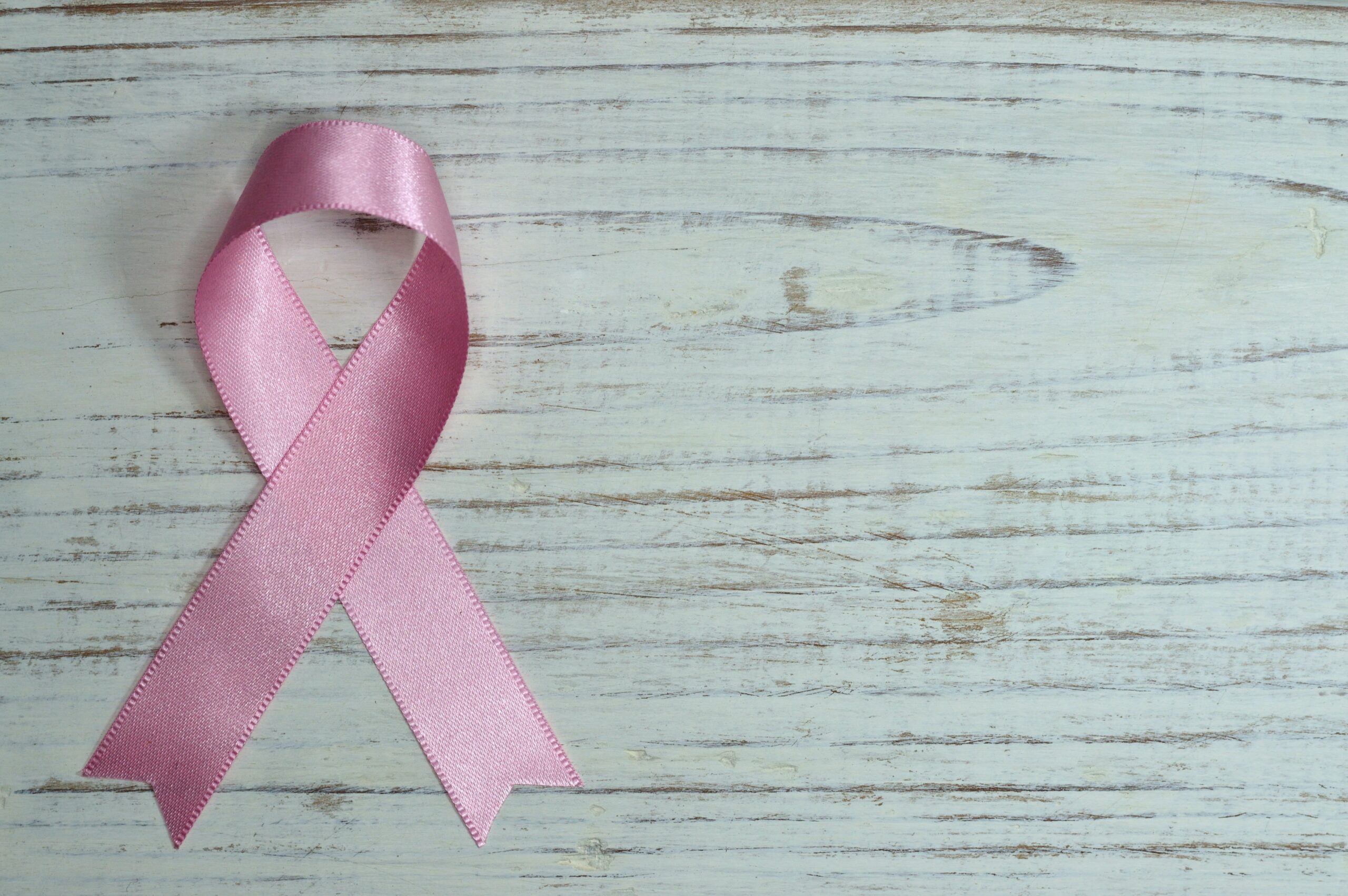 pink breast cancer pin badge on a white washed wooden background