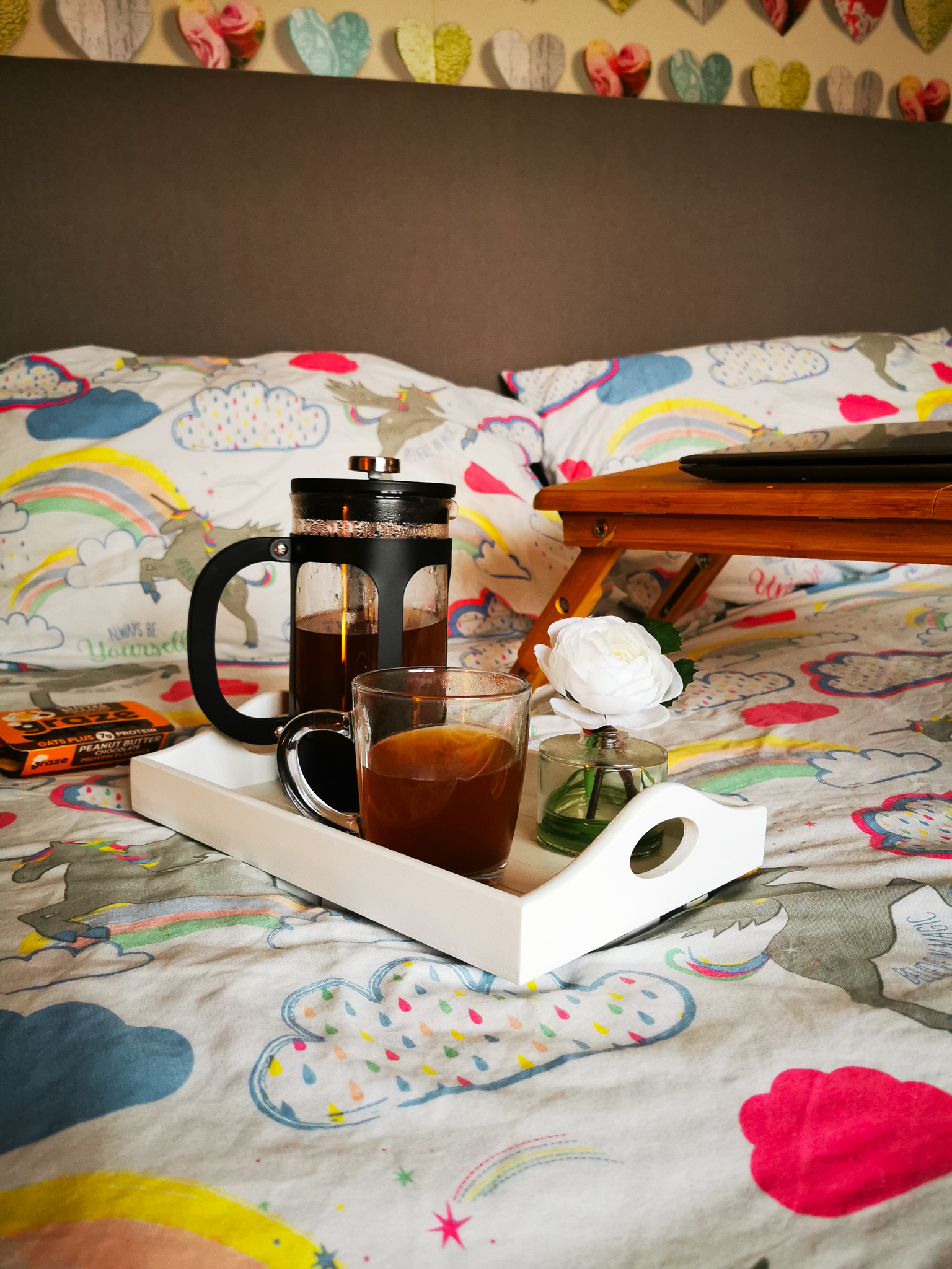 bed with a laptop table in view and sall white tray with a cafetiere and cup of coffee