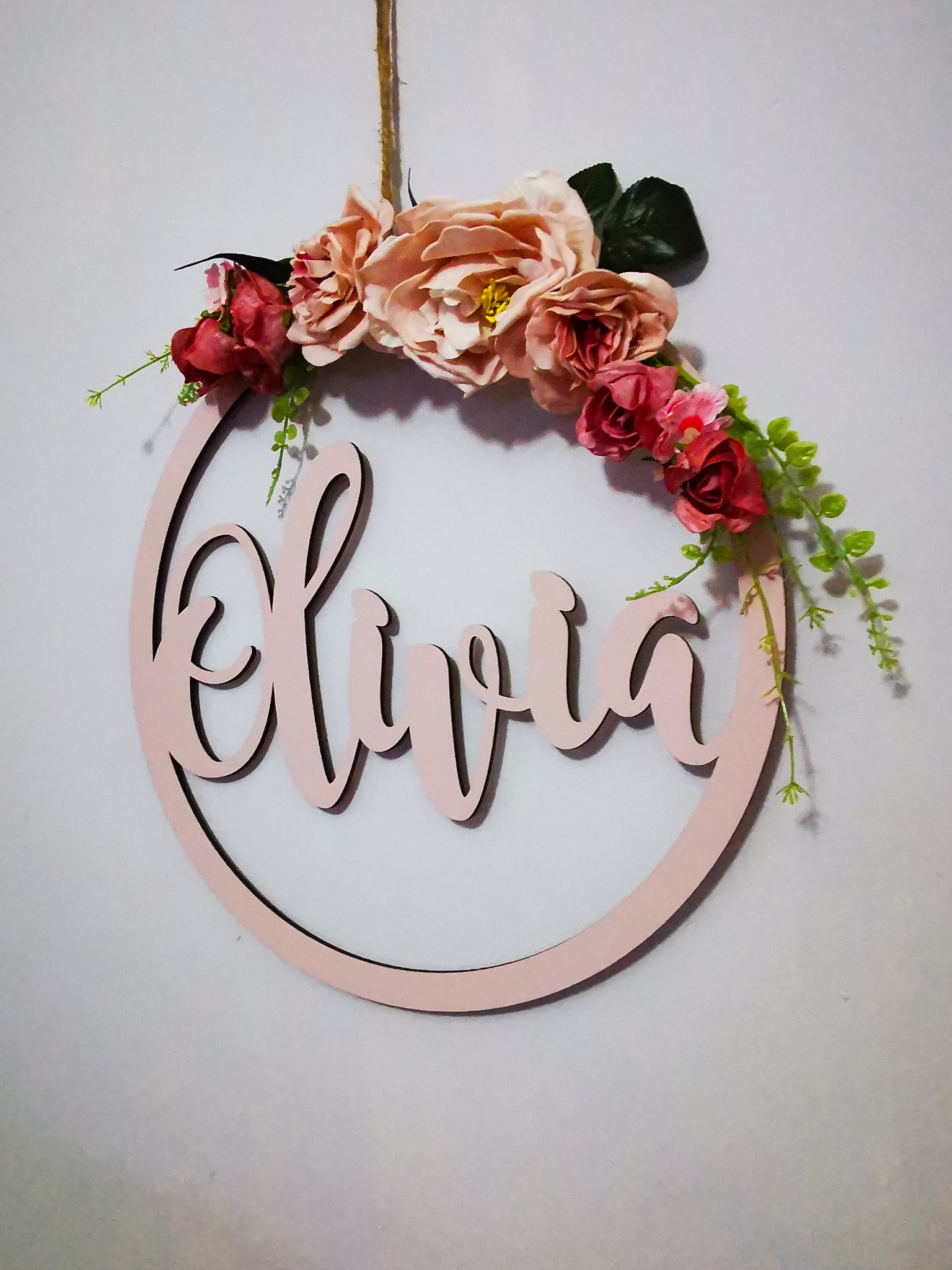 pink round wooden hoop on a white wall with the name olivia and flowers on the top of the hoop