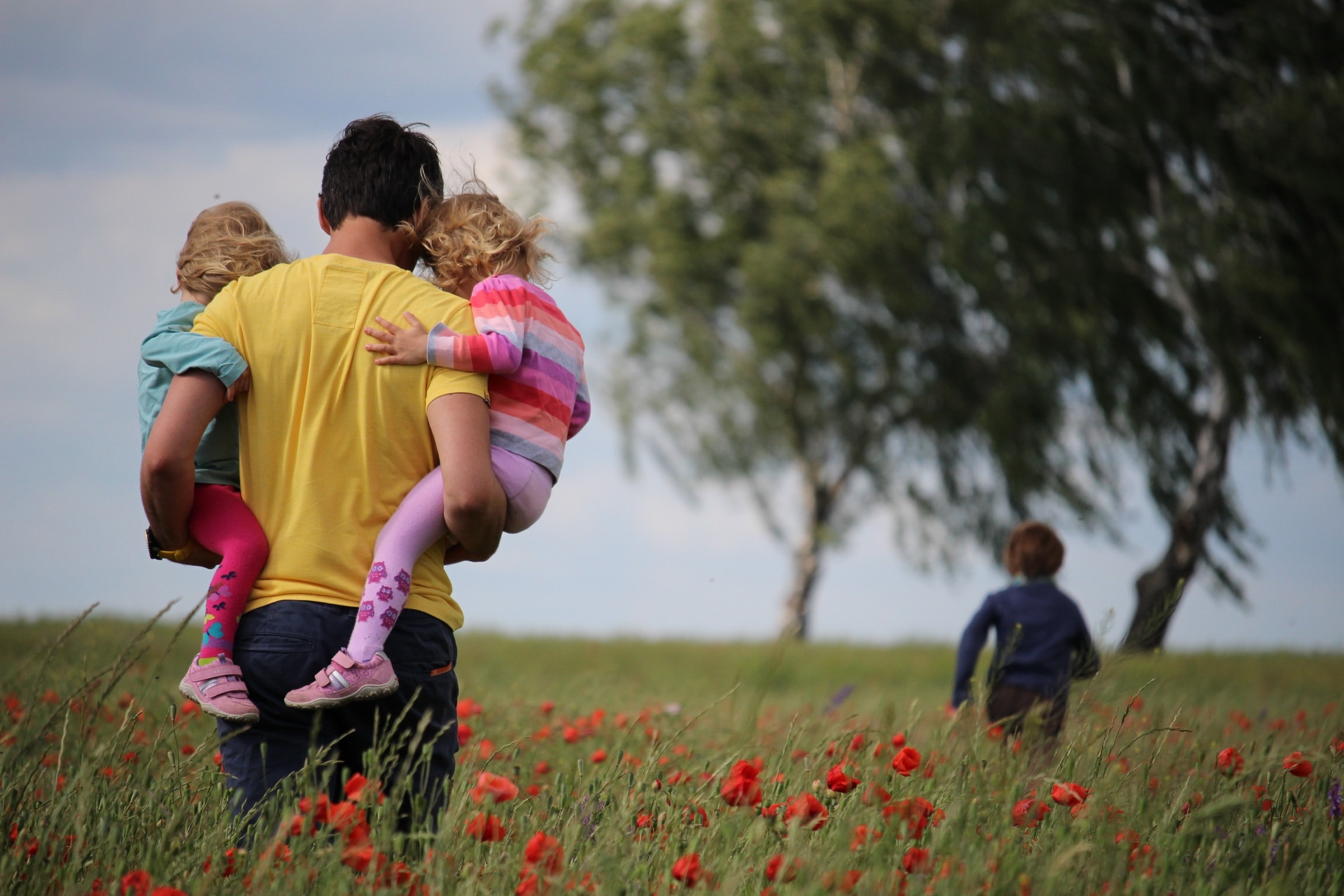 man holding two young children in a field