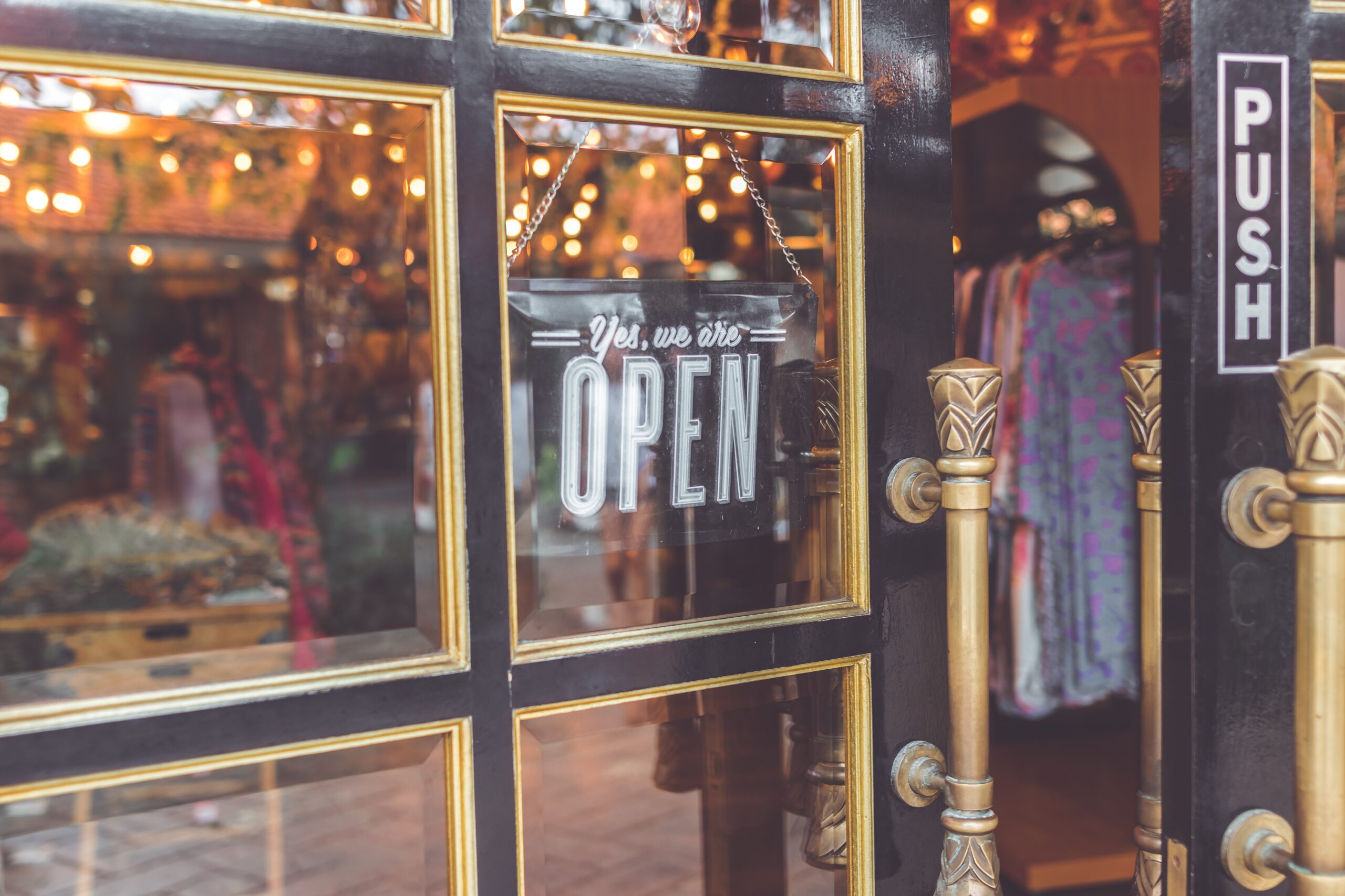 panelled door with a black we are open sign in the window with festive lights in the background