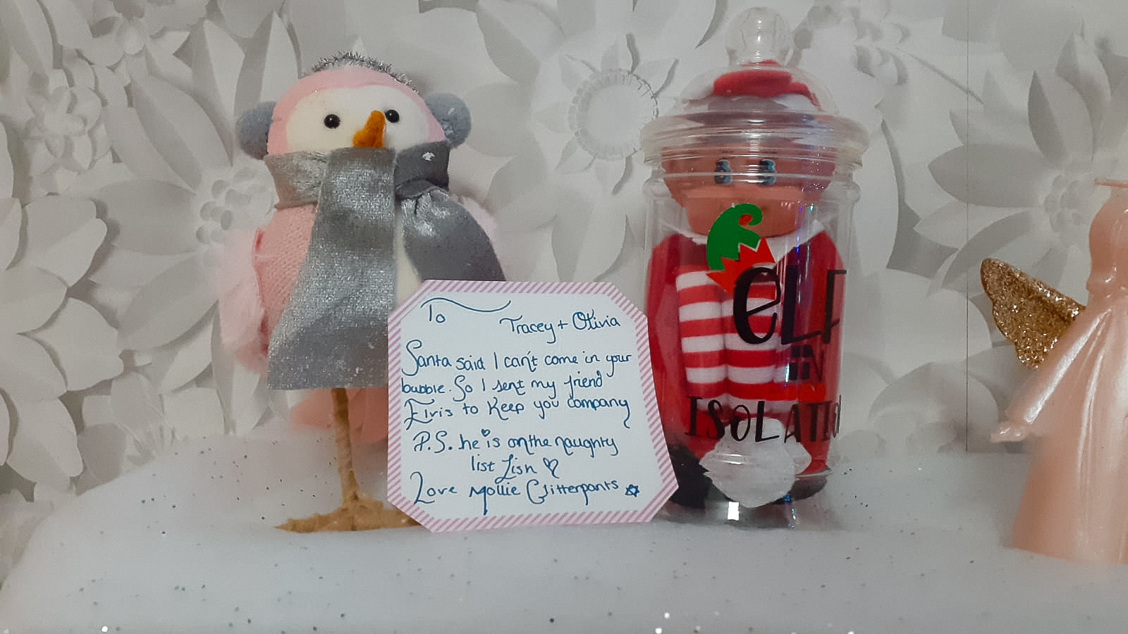elf on the shelf in an isolation jar surrounded by pink christmas decorations