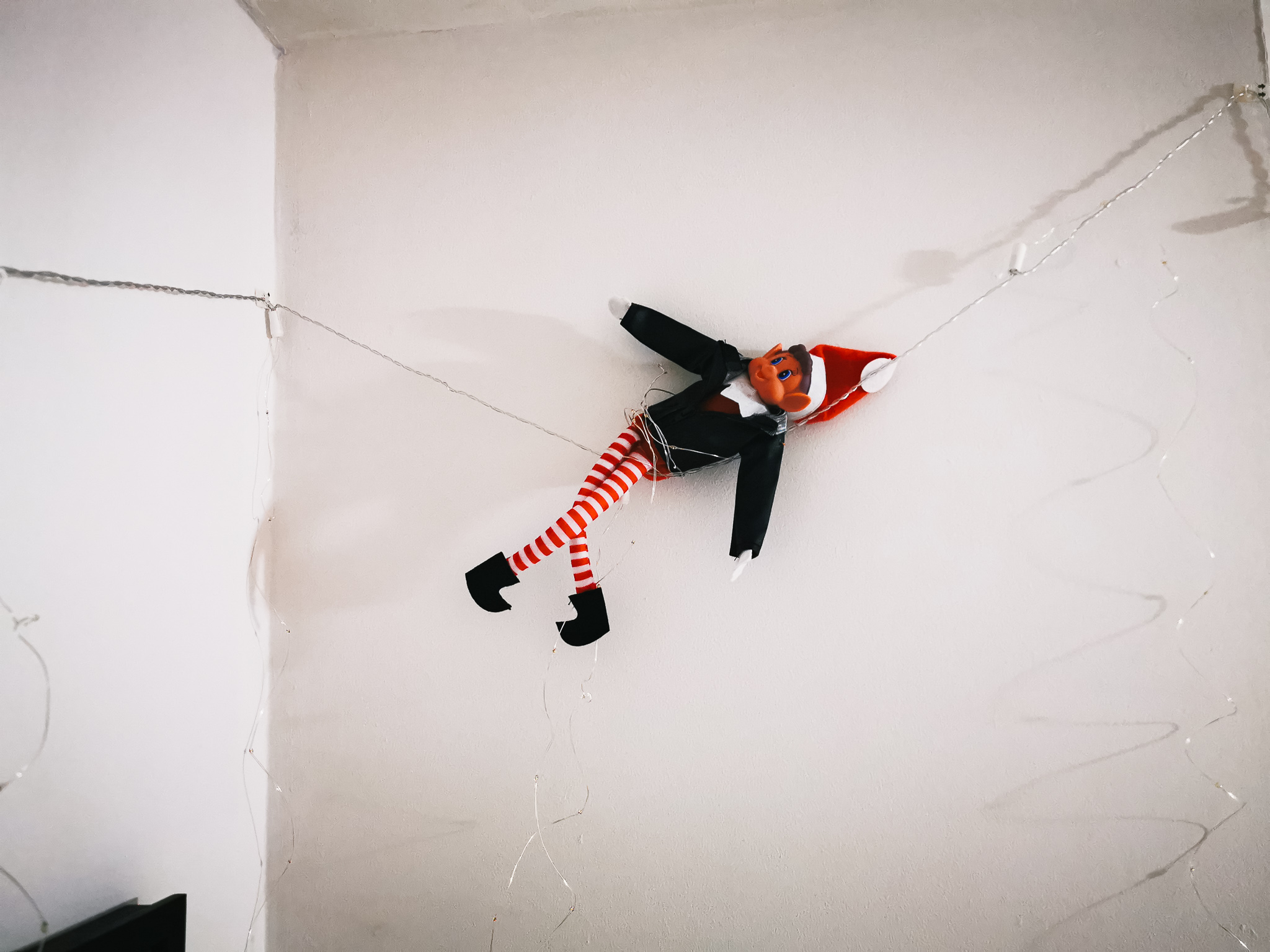 an elf wrapped in wire dangling against a white wall